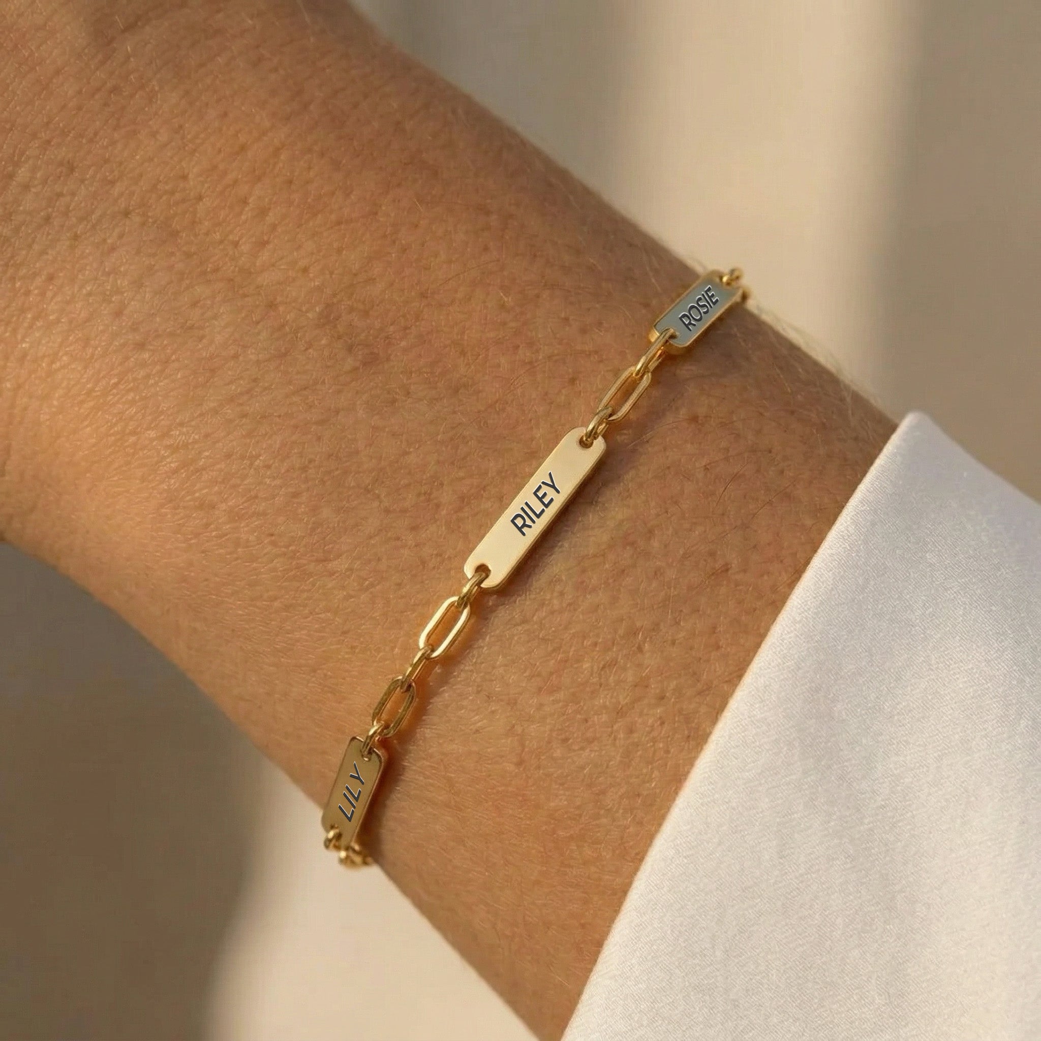 Gold paperclip chain pet name bracelet with three engraved name bars worn on a forearm