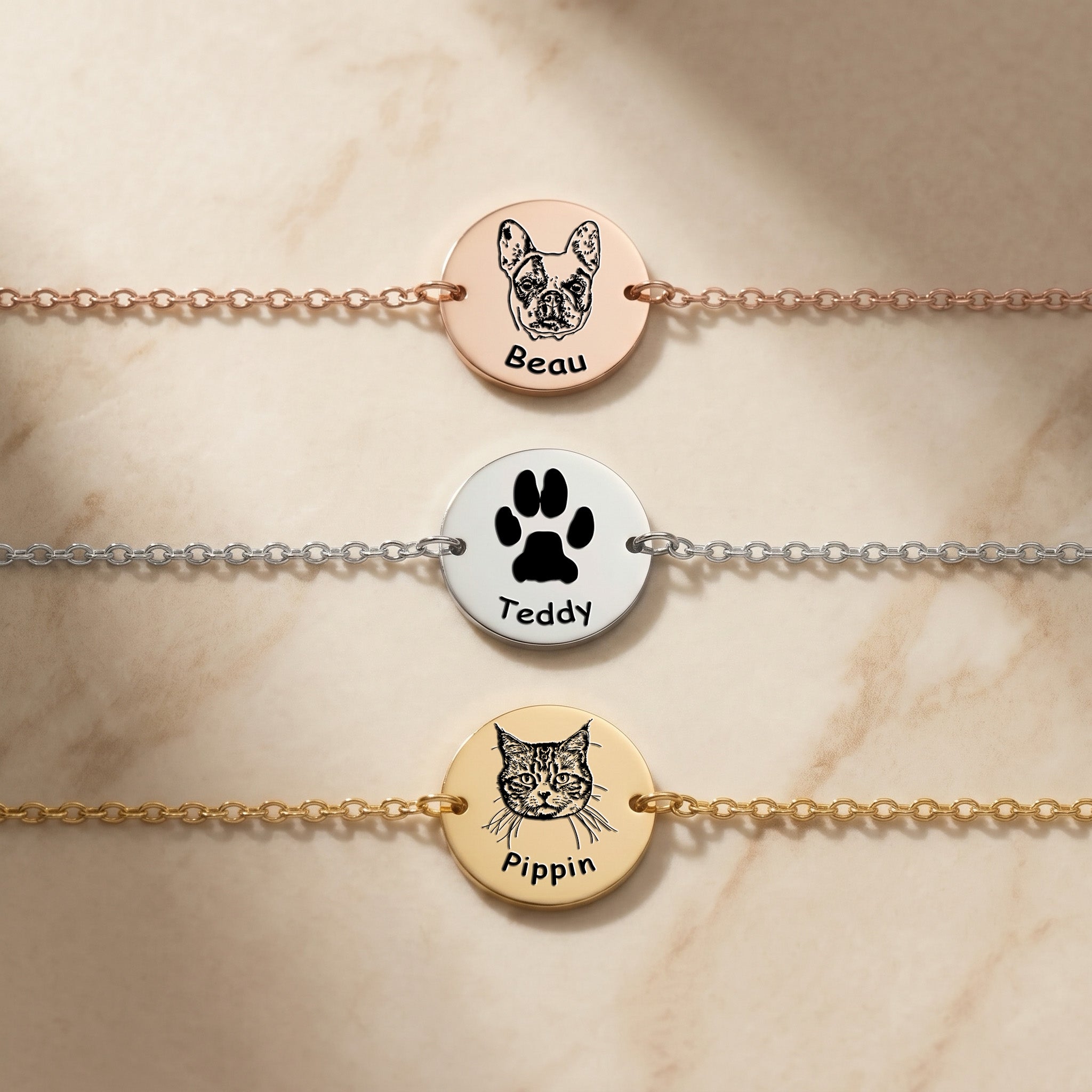 Three pet portrait chain bracelets on marble — rose gold with French Bulldog, rhodium with paw print, gold with cat — showing all three finishes and engraving styles