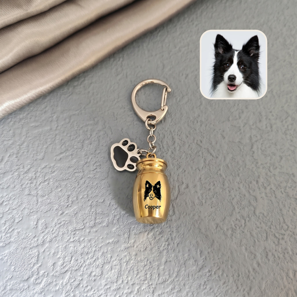 18k yellow gold pet urn keychain staged against a textured wall background with a dog reference photo inset, hand-drawn portrait engraved on the capsule face